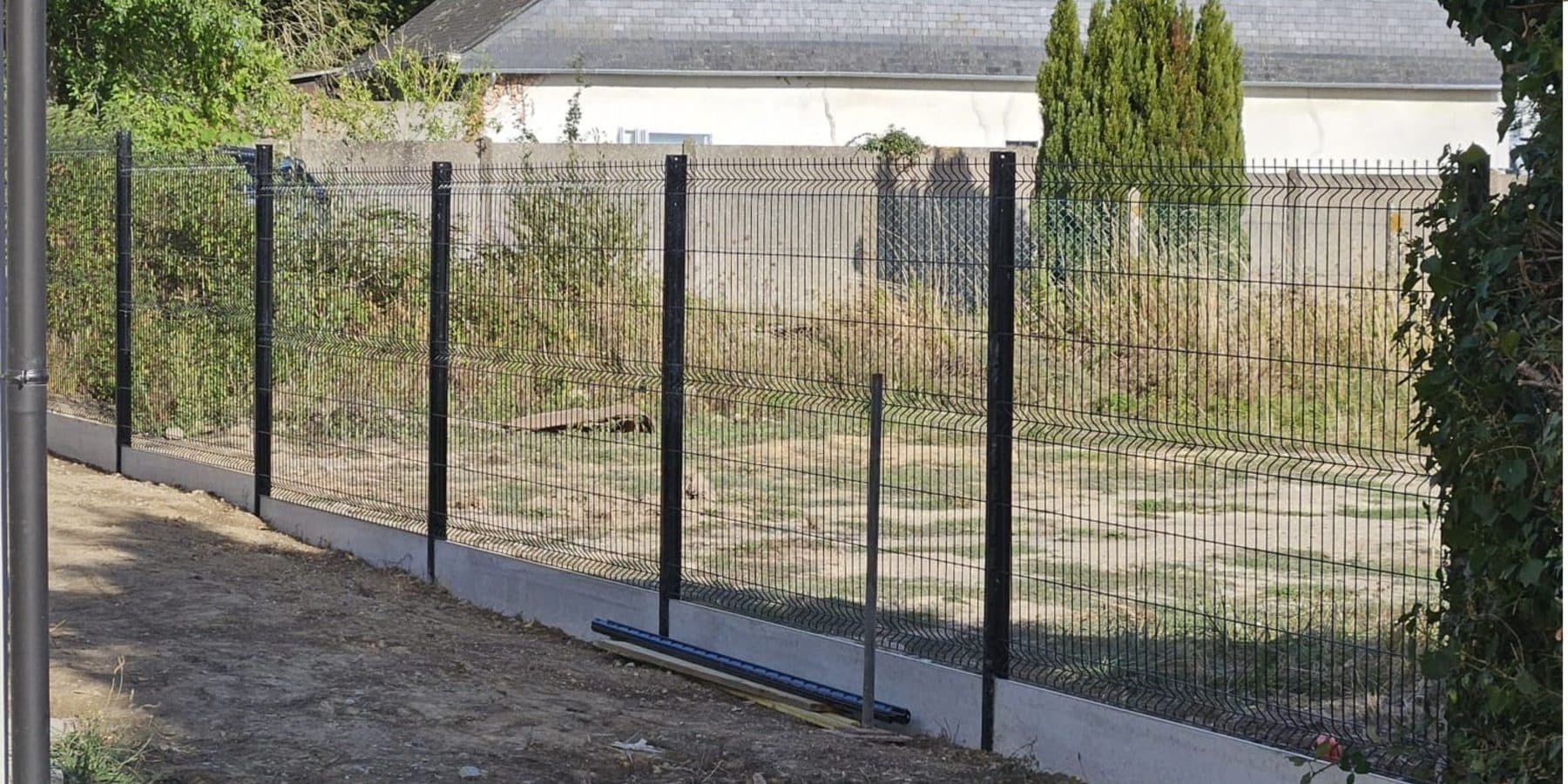 Clôture en grillage rigide anthracite posée sur plaques de soubassement béton le long d'un jardin, chantier à L'Hermitage